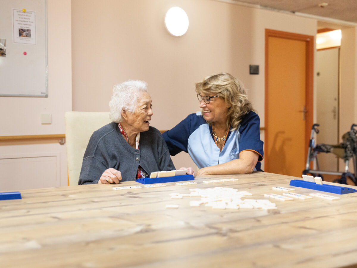 Een medewerker van Kennemerhart aan tafel met een bewoner, doen een spelletje rummikub.