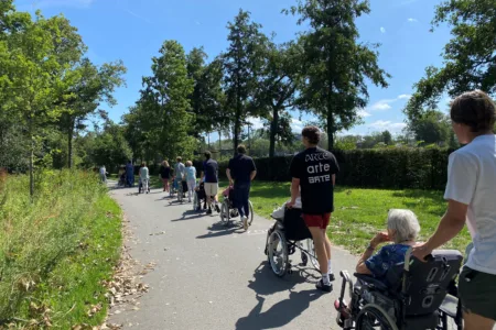Foto van een rij met medewerkers die achter clienten in rolstoel lopen