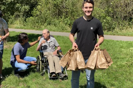 Foto jongen met tasjes in hand buiten op gras met client op achtergrond