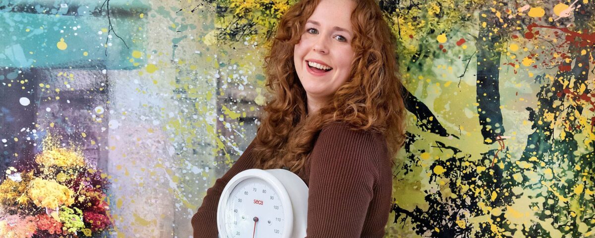 dietiste staat tegen muur geleund met weegschaal in handen