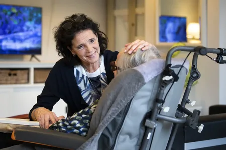 medewerker aait over hoofd client in rolstoel