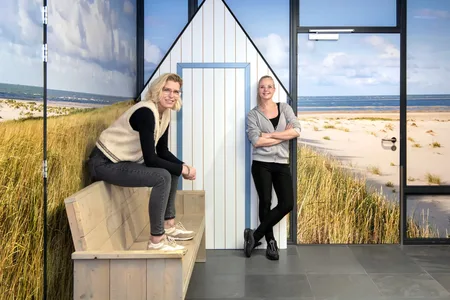 vrouw zit op bank met vrouw die leunt tegen de muur