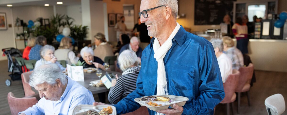 Man loopt met twee borden eten in eetzaal