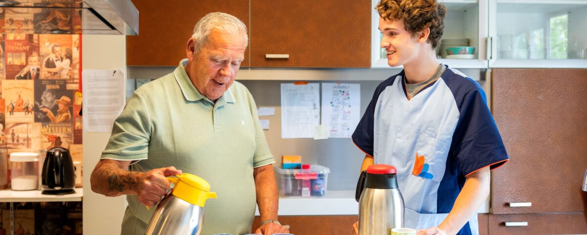 zorgmedewerker naast man in keuken met kannen