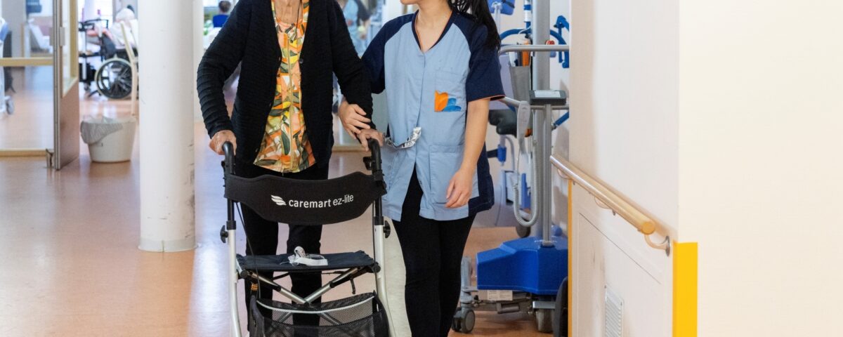 Dame met rollator op de gang met zorgmedewerker