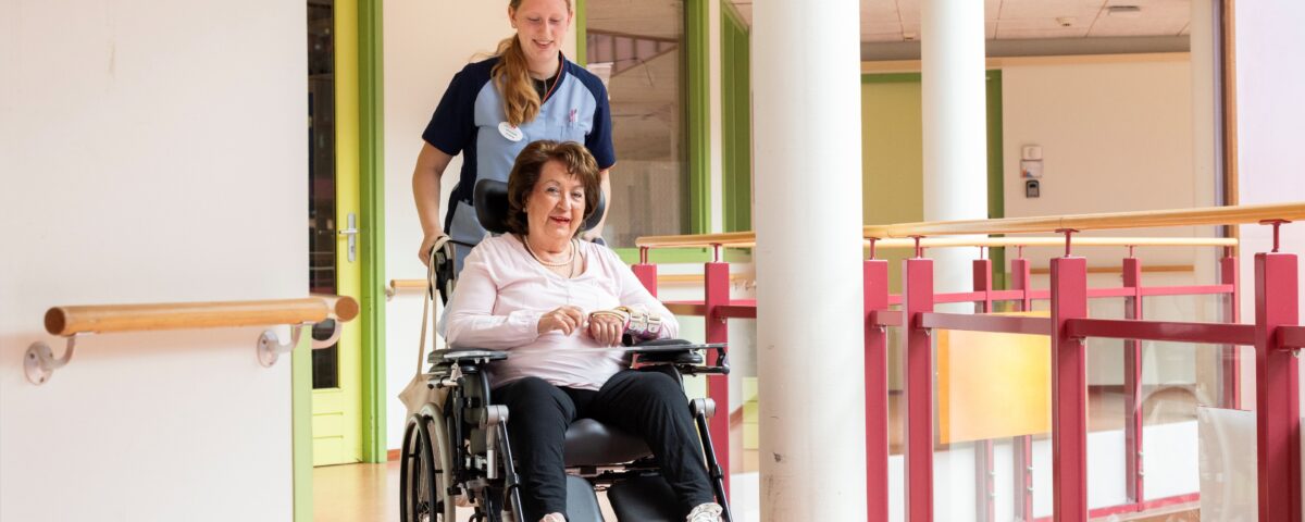 vrouw in rolstoel met zorgmedeweker er achter