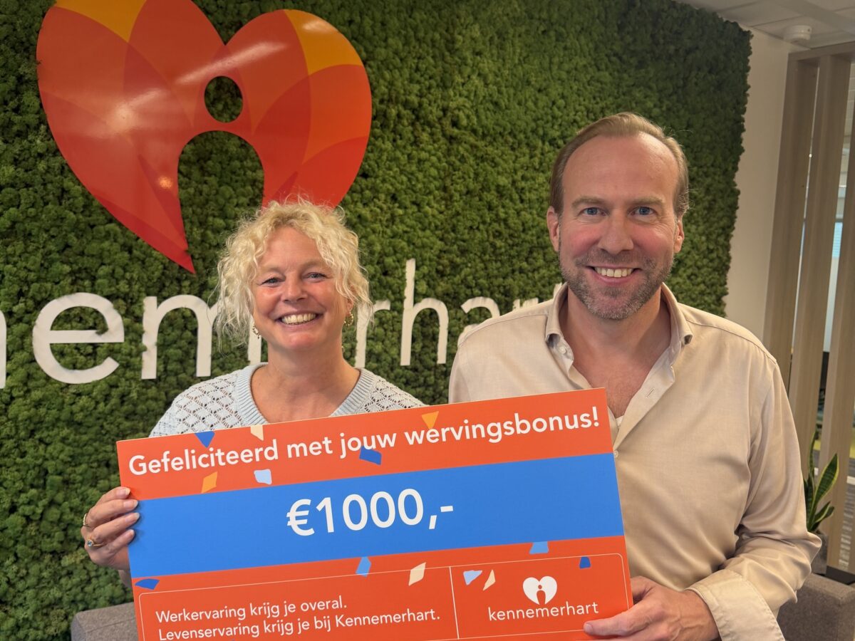 Twee collega's van Kennemerhart houden een cheque in de hand met tekst: Gefeliciteerd met jouw wervingsbonus! 1000 euro.