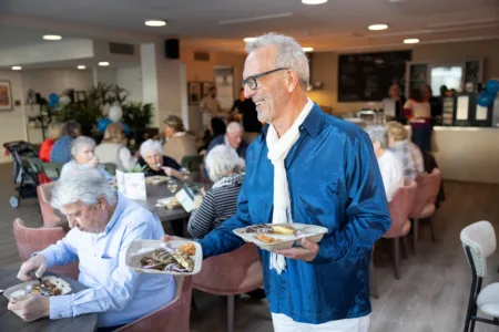 Man loopt met twee borden eten in eetzaal
