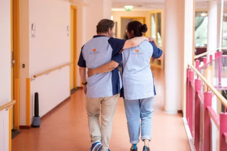 Twee zorgmedewerkers omhelzen elkaar op de gang