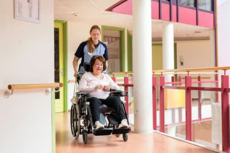 vrouw in rolstoel met zorgmedeweker er achter