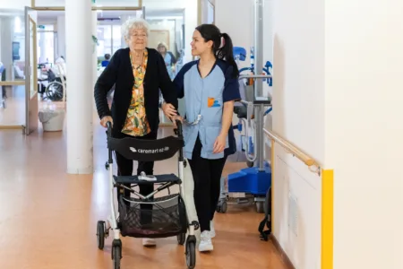 Dame met rollator op de gang met zorgmedewerker