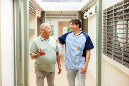 Zorgmedewerker met meneer op de gang